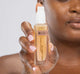 A woman is holding a bottle of FarmHouse Fresh Supremely Lit Serum-in-Oil with CBD that leaves skin glowing and dewy.