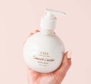 A hand holding a bottle of FarmHouse Fresh Sweet Cream Body Milk Lotion in a glass bottle with a pump top.