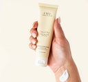 A hand holding a tube of Sweet Tea Shea Butter travel-size cream by FarmHouse Fresh scented with notes of peach, ginger, orchid and white tea.