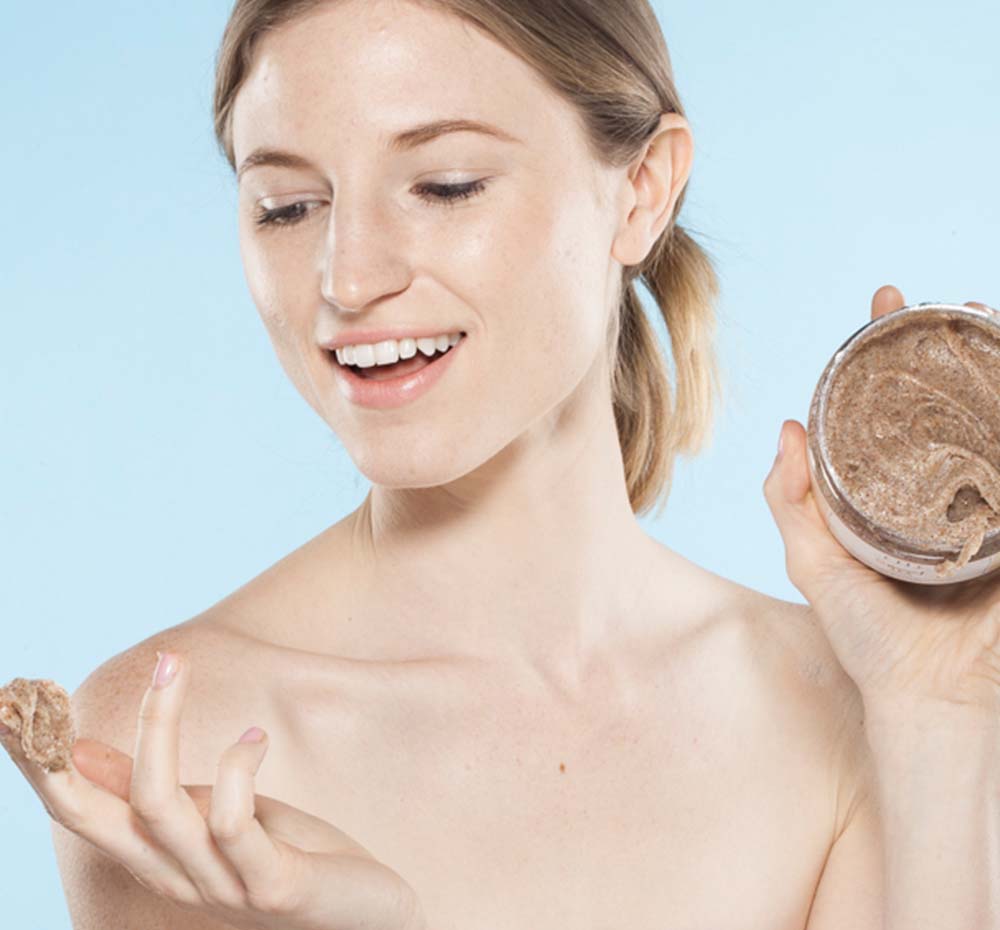 A woman is holding a jar of Sweet Tea gentle body scrub by FarmHouse Fresh scented with notes of peach, ginger, orchid and white tea.