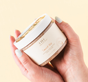 Hands holding a jar of Sweet Tea Whipped Shea Butter Body Polish by FarmHouse Fresh, a creamy, whipped, gentle cleanser that exfoliates with sugar grains and apricot seed powder.