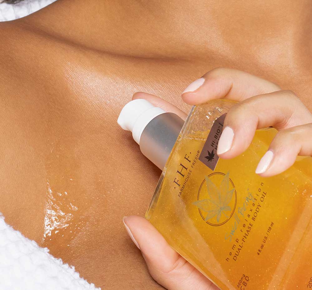 A woman is applying FarmHouse Fresh Swell Being Hemp Relaxation Body Oil with CBD on her body to nourish and soften her dry skin.