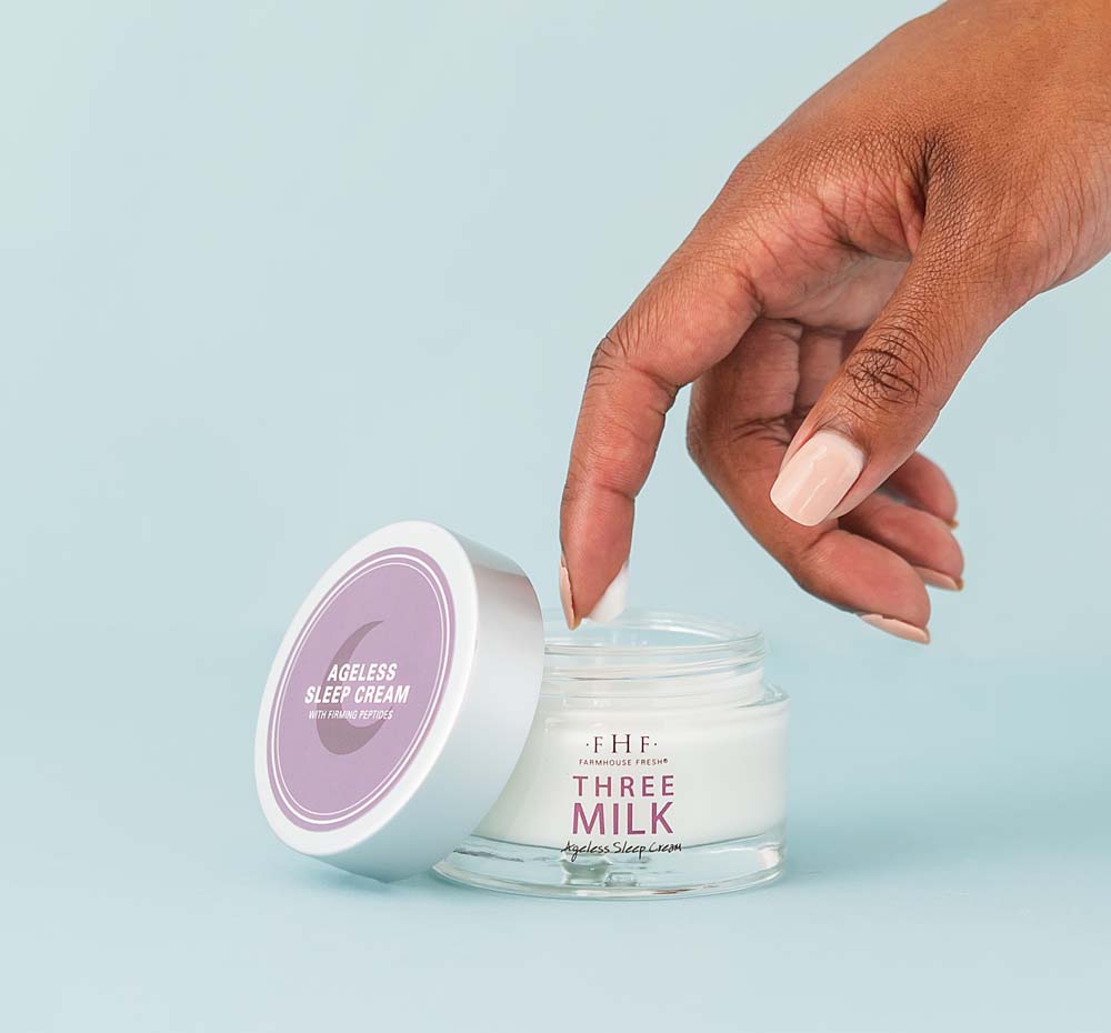 A woman is dipping her finger into the jar of FarmHouse Fresh Three Milk Ageless Sleep Cream with Peptides, a rich and deeply hydrating overnight moisturizer.