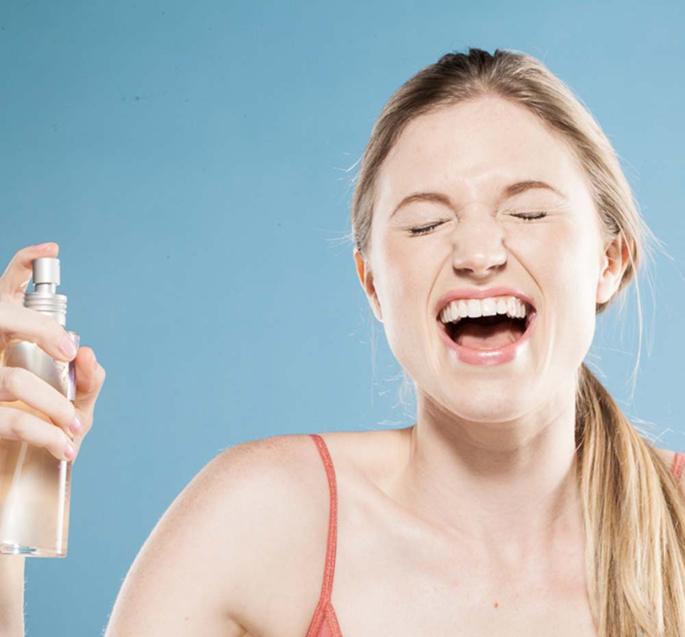 A woman smiling after misting her face with Vitamin Berry Facial Tonic FarmHouse Fresh, a refreshing face toner for dry skin that erases the appearance of enlarged pores.