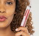 A woman is holding FarmHouse Fresh Vitamin Glaze Oil Infused Lip Gloss in Berry color, demonstrating the bright and sassy color.