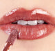 A woman is applying FarmHouse Fresh Vitamin Glaze Lip Gloss in Brick color that brings color and hydrates lips.