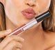 A woman holding FarmHouse Fresh Vitamin Glaze Oil Infused Lip Gloss in Brick color by her face, demonstrating the rich color of the lip gloss and her soft, well moisturized lips.