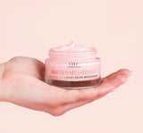 Hand holding a jar of Farmhouse Fresh Watermelonaid cream infused with watermelon extract and CBD on a pink background.
